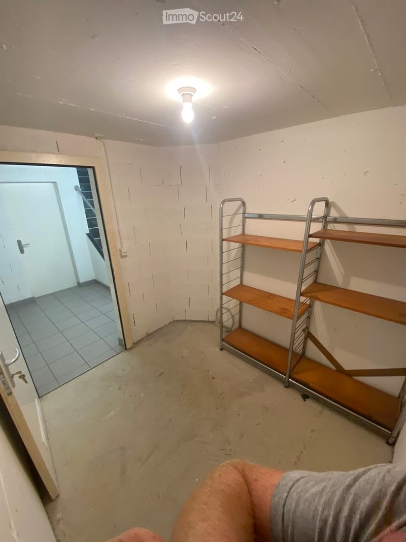 Empty room with concrete floor, white walls, a single shelf unit, and a doorway leading to another tiled area.