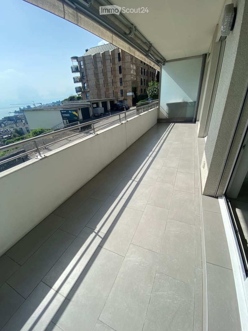 Balcony with tiled floor, metal railing, and a view of a modern building and waterfront.