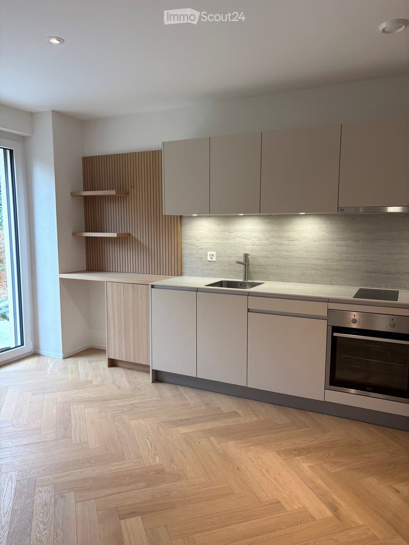 Modern kitchen with light wood cabinets, stainless steel appliances, and a marble backsplash.