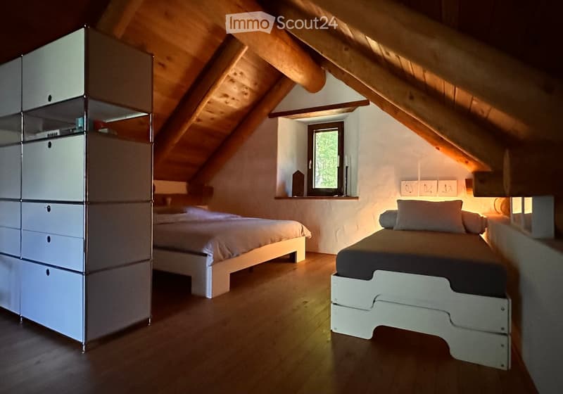 Cozy attic bedroom with wooden slanted ceilings, two single beds, a modern wardrobe, and a small window with a view of greenery.