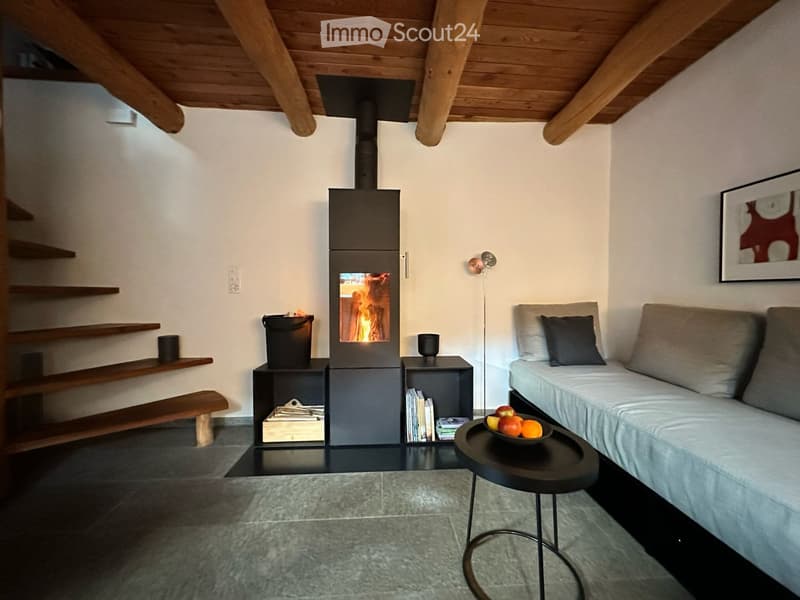 Modern living room with exposed wooden beams, a central fireplace, a grey sofa, a round coffee table, and a floor lamp.