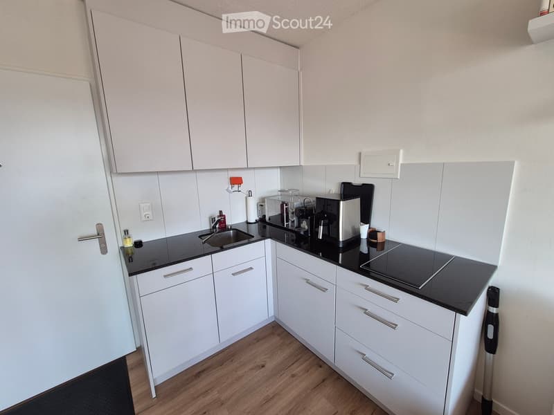 Modern kitchen with white cabinets, black countertops, and stainless steel appliances including a coffee maker and oven. Features a sink with a faucet and a bottle on the counter.