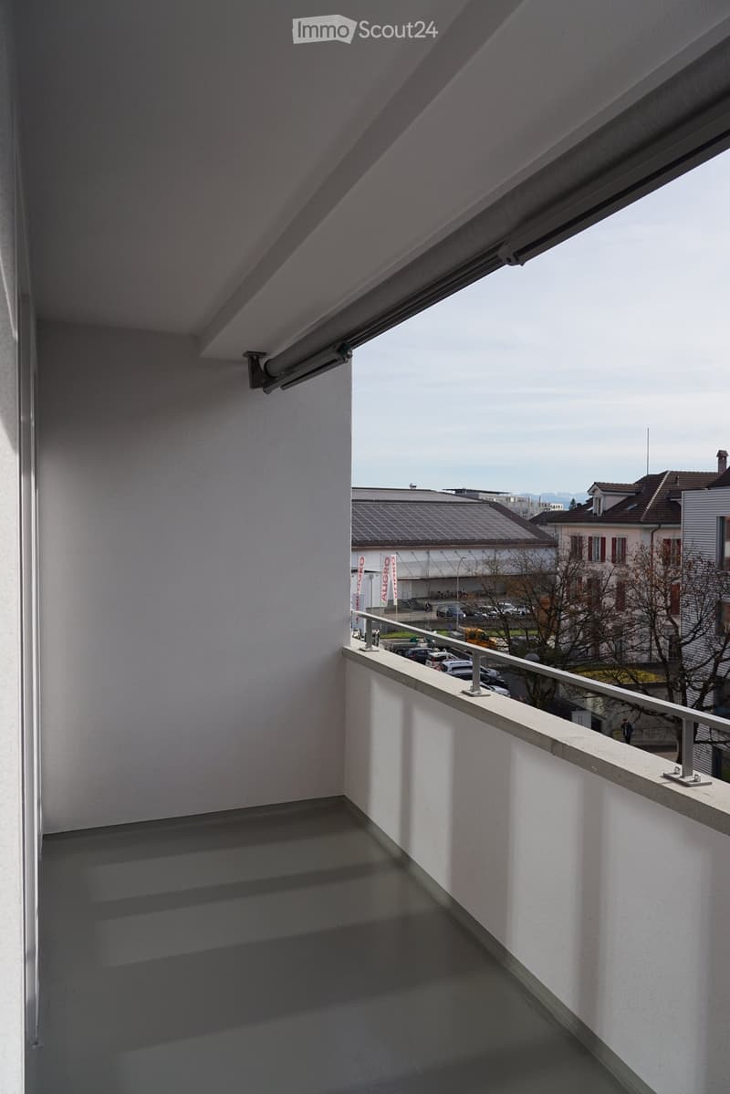 The balcony has a view of a city with buildings and cars, along with solar panels and mountains in the distance.