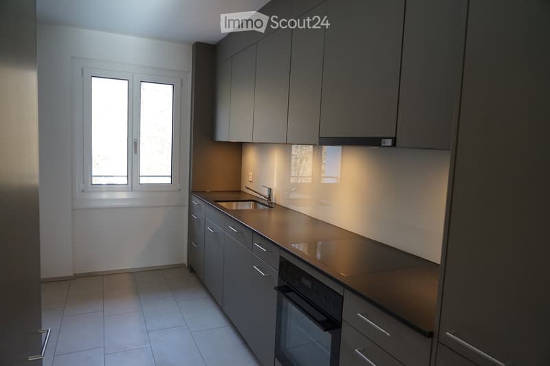 Kitchen with tiled floor, under cabinet lighting, double glass door window, stainless steel sink with faucet, built-in dishwasher and washing machine, cabinets, and black countertops.