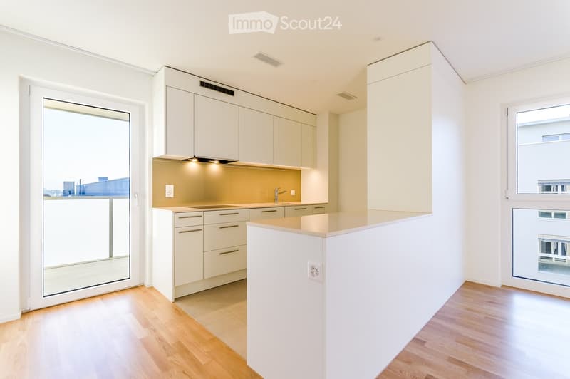 Modern kitchen with white cabinets, a central island, and a sleek countertop. Features a built-in sink and faucet, with large windows providing natural light.