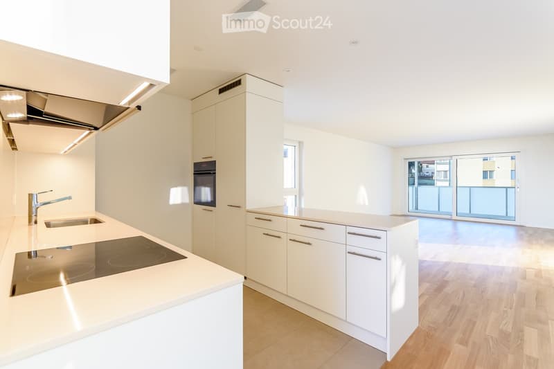Modern kitchen with white cabinets, a central island, an induction cooktop, a sink with a modern faucet, and an oven. Large windows and sliding doors lead to a balcony.