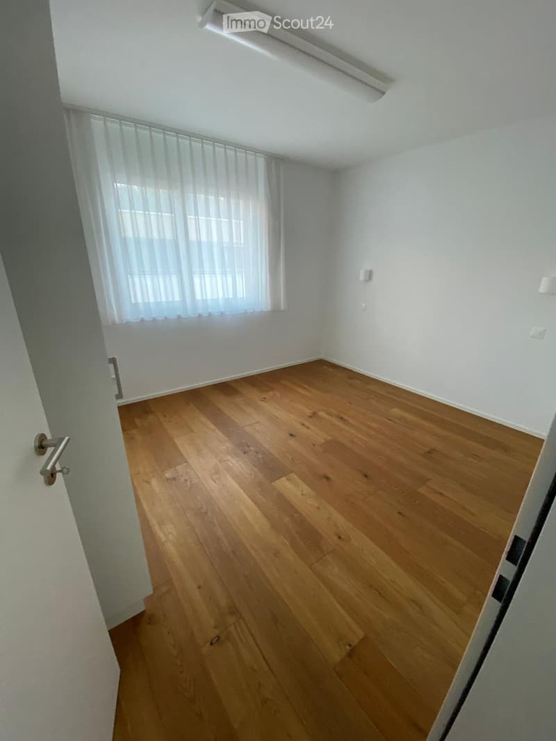 Empty room with wooden flooring, white walls, and a window with sheer curtains. No furniture or equipment is present.