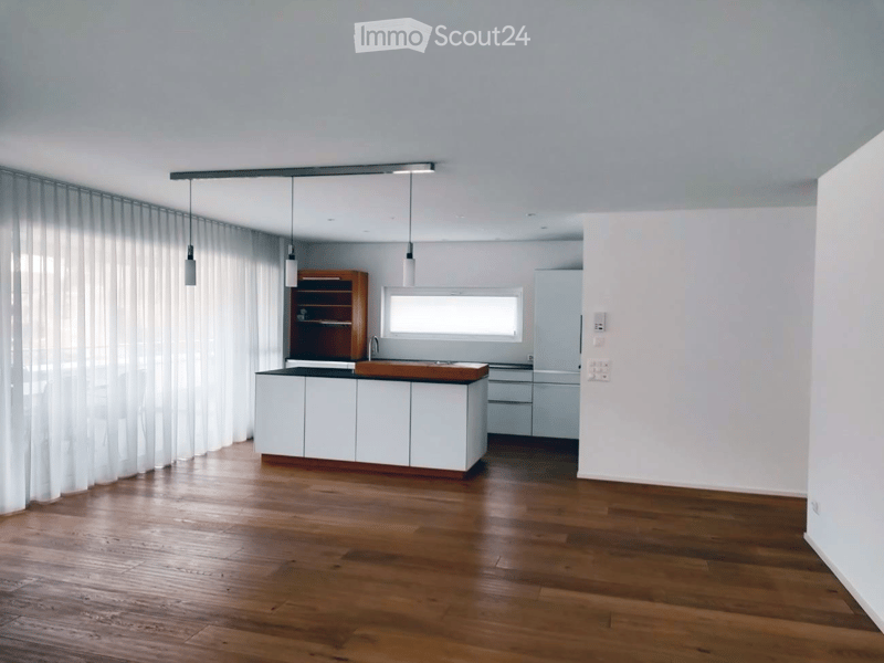Modern kitchen with white cabinets, wooden countertop, and pendant lights. Features a wooden shelf, a sink with a faucet, and a refrigerator. The space is illuminated by natural light from a window covered with sheer curtains.