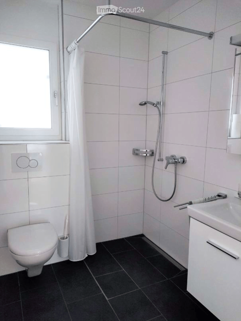 Modern bathroom with white tiles, black floor, shower with curtain, toilet, sink, and toothbrush holder.