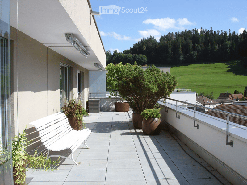 Balcony with white bench, potted plants, and scenic view of green fields and trees.