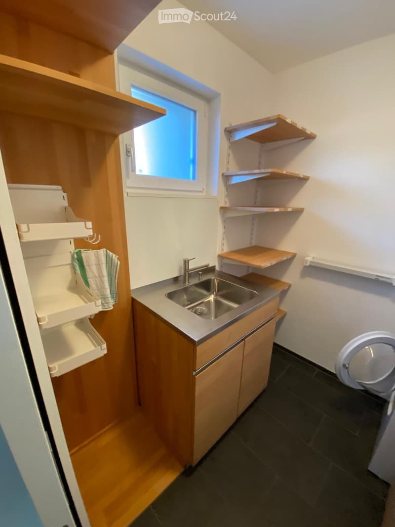 Compact kitchen with wooden cabinets, stainless steel sink, shelves, and a towel hanging on the side.
