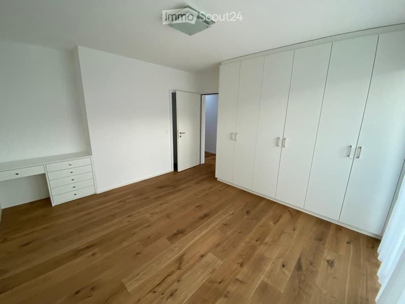 Empty room with light wooden flooring, white walls, built-in white wardrobes, and a small built-in desk with drawers.