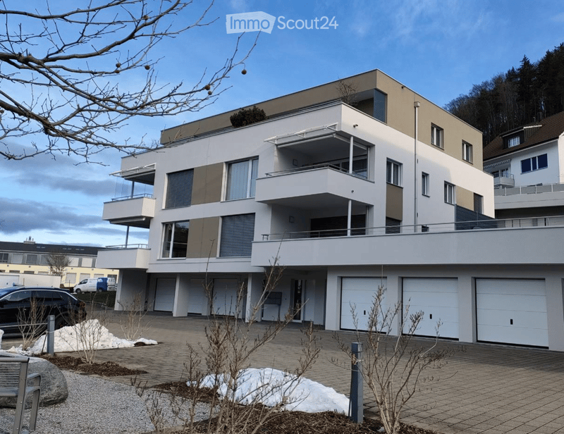 Modern two-story house with white and beige facade, multiple balconies, large garage, and contemporary design.