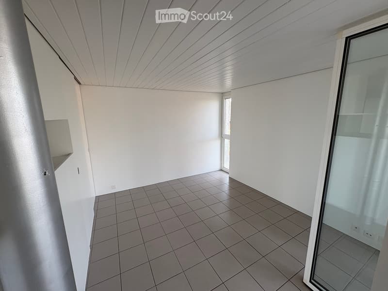 Empty room with white walls, tiled floor, and large window with blinds. No furniture or equipment visible.