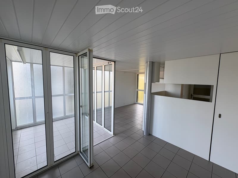 Empty room with tiled floor, large glass sliding doors, white walls, and a white partition in the corner.