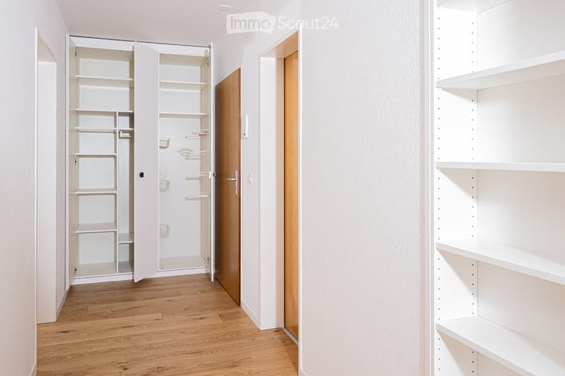 Empty room with wooden flooring, white walls, and built-in white shelving units with multiple open compartments and shelves.