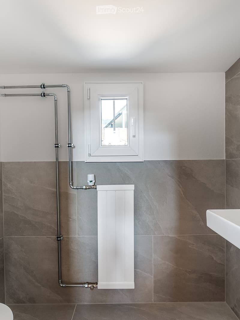 Modern bathroom with grey marble tiles, white radiator, and a window with white frame.