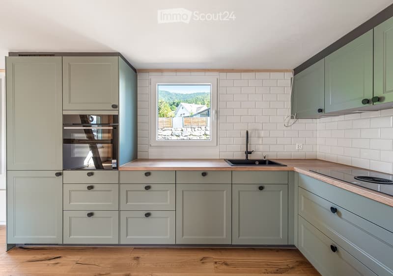 Modern kitchen with light grey cabinets, wooden countertops, and a window overlooking a scenic outdoor view.