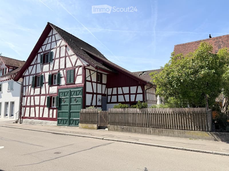 Traditional half-timbered house with white and red exterior, green shutters, and a wooden fence in front.