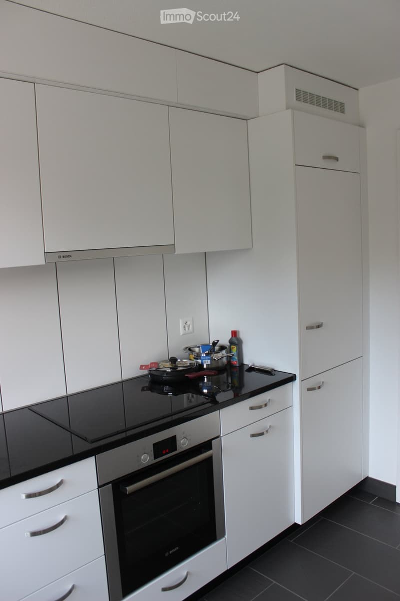 Modern kitchen with white cabinets, black countertop, built-in oven, and various kitchen items on the counter.