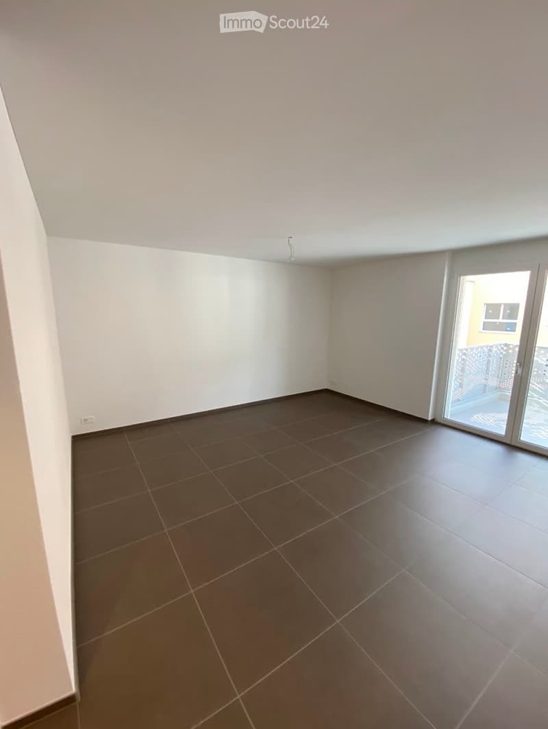 Empty room with tiled floor and white walls, featuring a large sliding glass door leading to a balcony.