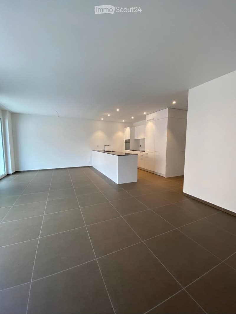 Modern, minimalist kitchen with white cabinets, a central island, and dark tiled flooring.