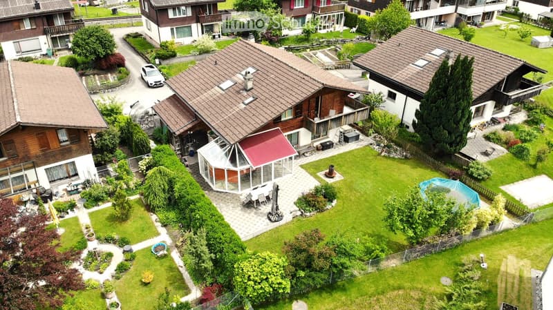 Aerial view of a residential area with multiple houses, well-maintained gardens, a swimming pool, and outdoor seating areas.