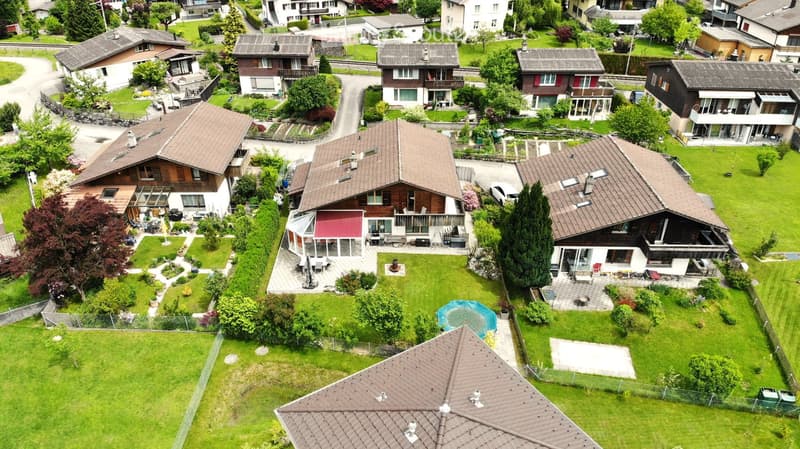 Aerial view of a residential neighborhood with multiple houses, well-maintained gardens, and a small swimming pool in one of the yards.