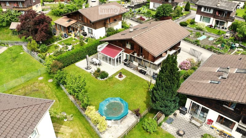 Aerial view of a residential area with multiple houses, gardens, and a swimming pool in the foreground.