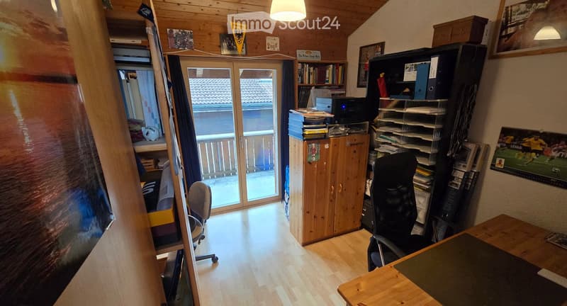 A well-furnished room with wooden flooring, a large window with a view, a desk with a chair, a cabinet, a bookshelf, and a printer on top.