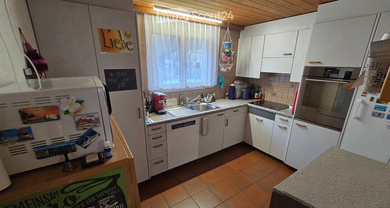 Modern kitchen with white cabinets, granite countertops, stainless steel appliances, and a window with sheer curtains.