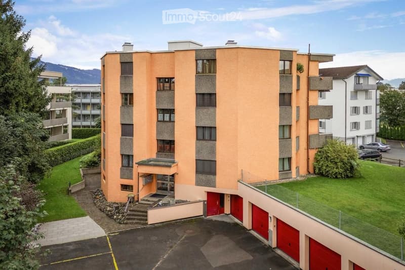 Multi-story residential building with orange facade, multiple windows, balconies, and a parking area with red garage doors.