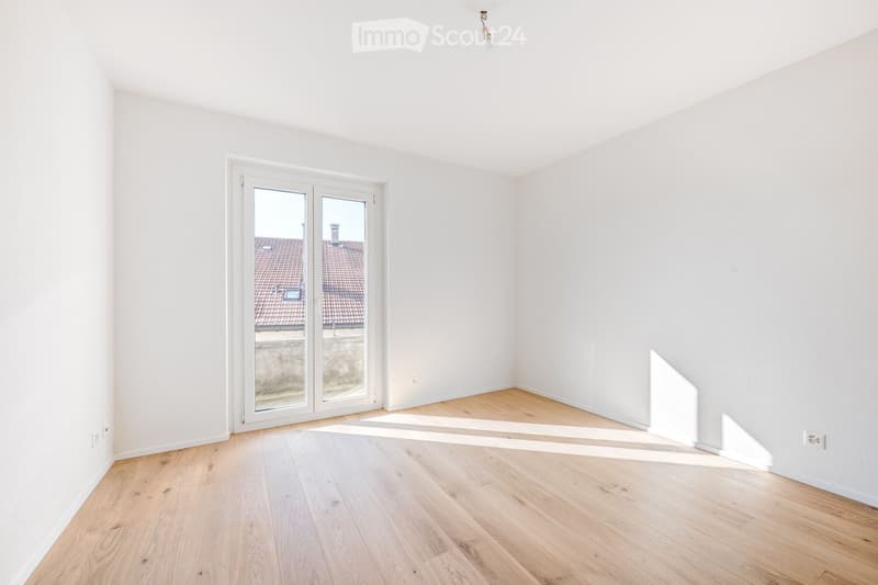 Empty room with white walls, wooden flooring, and large sliding glass doors leading to a view of a tiled roof.