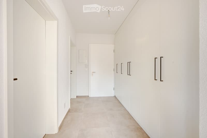 A clean, modern hallway with white walls, tiled floor, and several doors and cabinets.