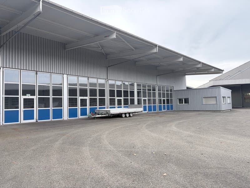 Large industrial building with a metal exterior, large glass windows, and a trailer parked in front.