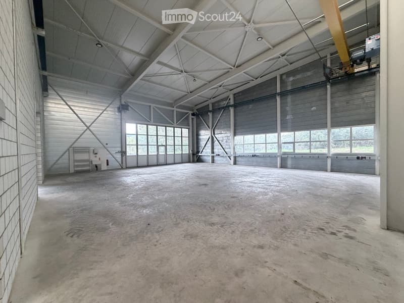 Large, empty industrial-style space with a high, metal-framed ceiling, concrete floor, and large windows along one wall. The room is completely unfurnished with no visible furniture or equipment.