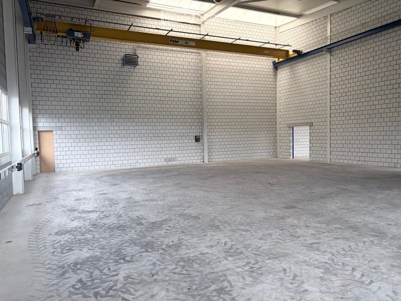 Empty industrial-style room with white tiled walls, concrete floor, and minimal structural elements.