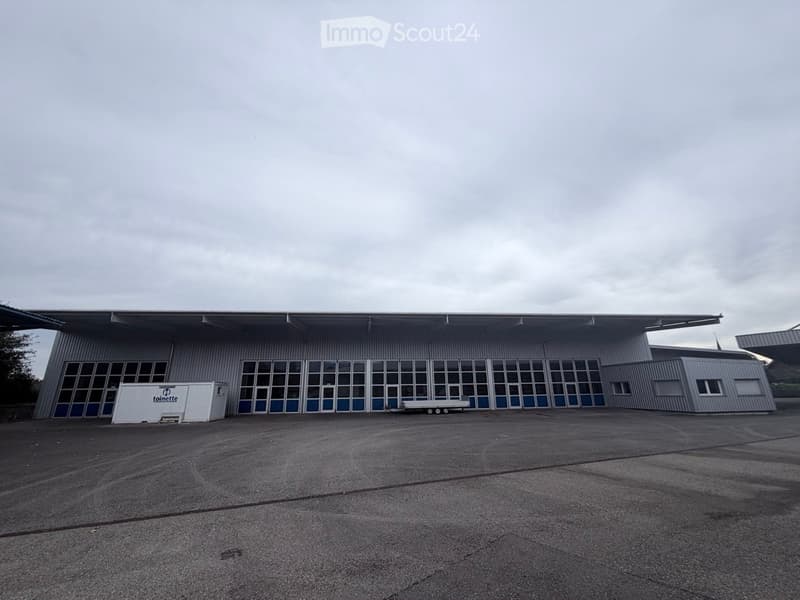 Large industrial-style building with a flat roof, extensive glass windows, and a container parked in front.