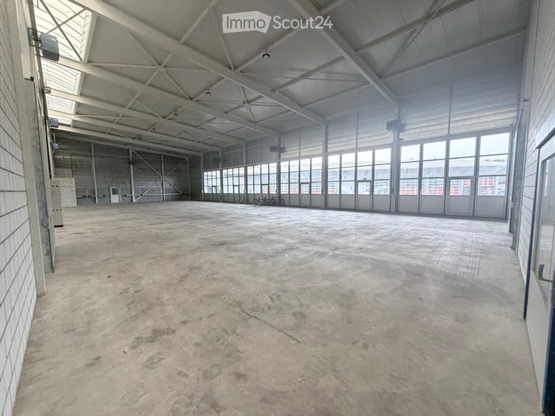 Large, empty industrial-style space with concrete floor, high ceilings, exposed metal beams, and large windows allowing natural light.