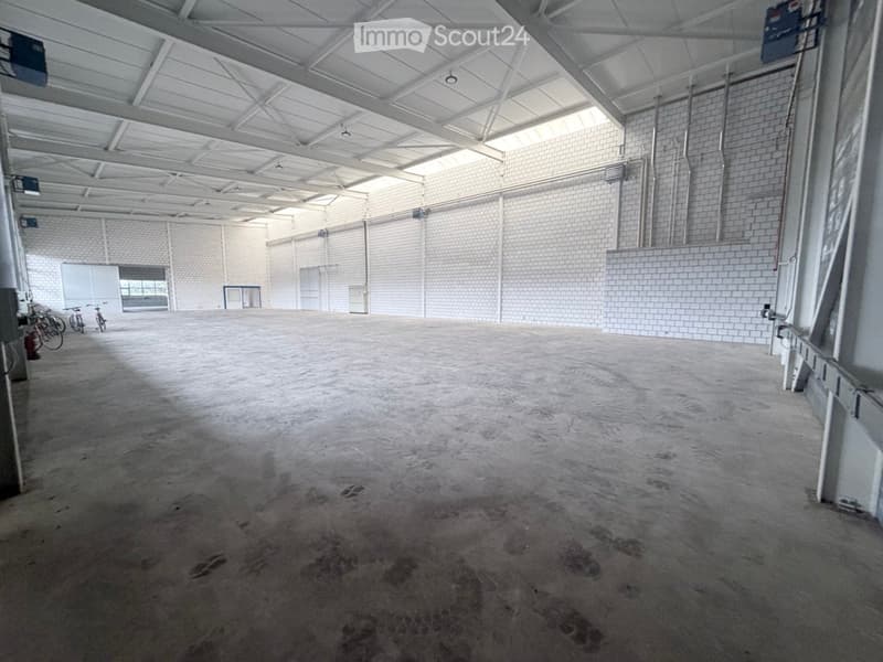 Large, empty industrial-style space with concrete floor, white brick walls, and metal ceiling structure. Minimal furnishings include a few bicycles and a small cabinet.