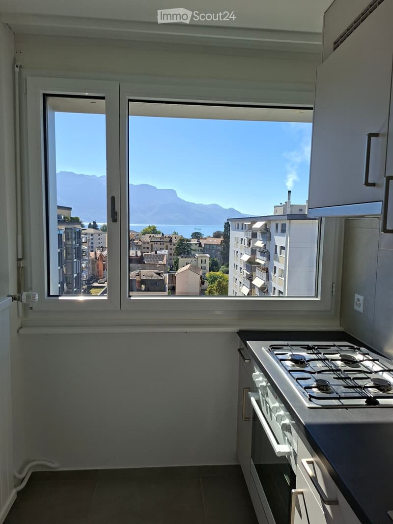 Modern kitchen with gas stove, white cabinets, and large windows offering a scenic view of mountains and a lake.