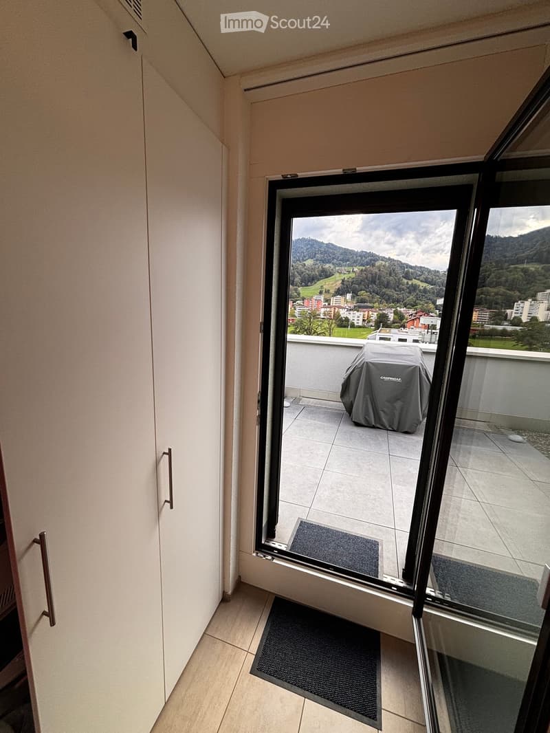 Open sliding glass door leads to a tiled balcony with a covered grill and a scenic mountain view.