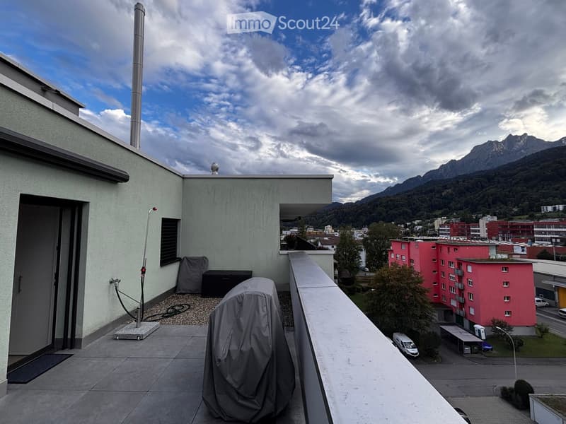 Balcony with a view of mountains and cityscape, featuring a covered object and a railing.
