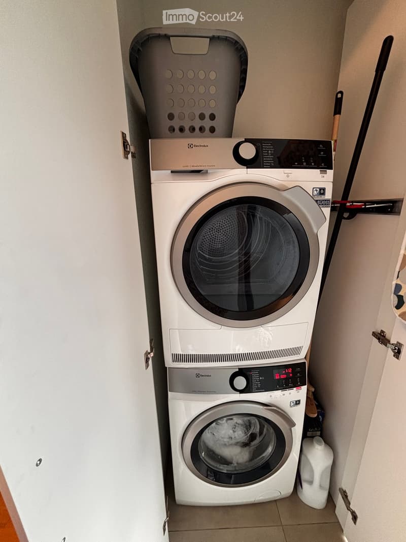 A compact bathroom with a stacked washing machine and dryer unit, featuring a control panel and a drum paddle.