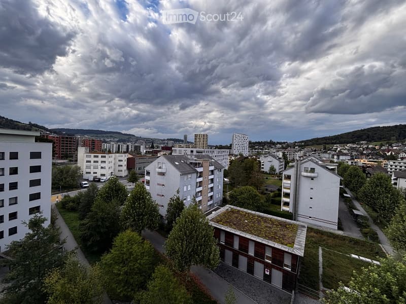 A panoramic view of a residential area with multiple apartment buildings, trees, and a cloudy sky in the background.
