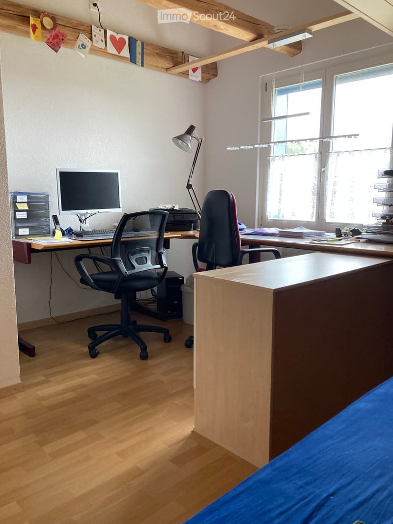 Office space with wooden flooring, two desks, two chairs, a computer screen, keyboard, printer, and a lamp.