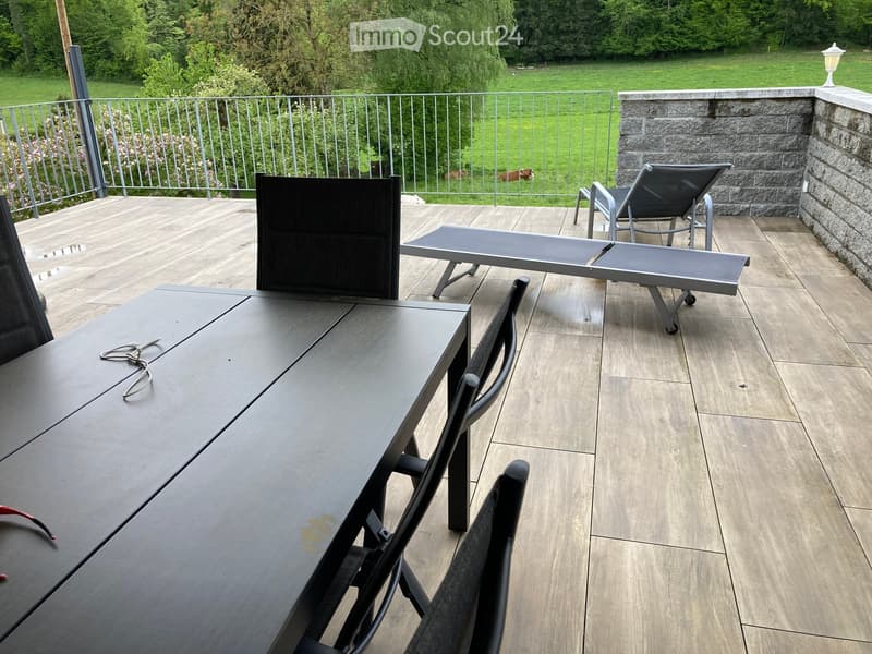 Balcony with wooden decking, metal railing, and outdoor furniture including a table, chairs, and lounge chairs.