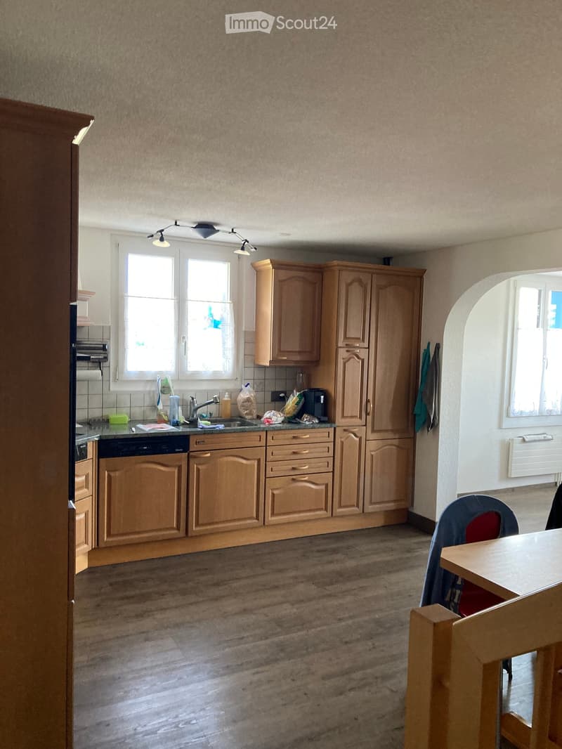 A well-lit kitchen with wooden cabinets, a sink, a dishwasher, and a small dining area with a table and chair.
