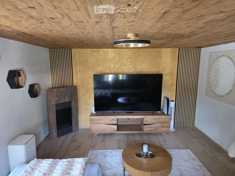 Modern living room with a large flat-screen TV on a wooden stand, a fireplace, a round coffee table, and wall-mounted lamps.