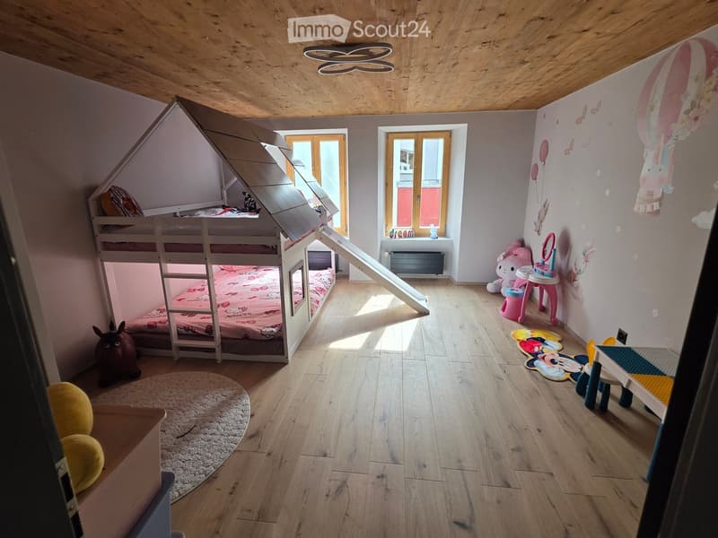 Cozy children's bedroom with wooden floors, bunk bed, slide, colorful toys, and wall decorations.